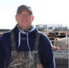 man wearing a hat standing in front of cows